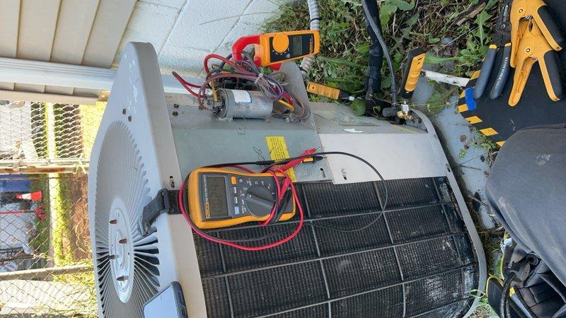 Responded to service call for central air conditioning unit repeatedly blowing fuses after 1-2 hours of operation. Upon arrival, accessed 10+ year old outdoor condensing unit located in backyard. Performed comprehensive electrical diagnostics using clamp meter and multimeter to measure amperage draw, voltage, and resistance across compressor, condenser fan motor, and capacitor circuits. Testing revealed abnormal electrical readings indicating potential compressor short cycling or capacitor failure causing excessive current draw and subsequent fuse failure. Documented electrical measurements and equipment condition with photos showing active diagnostic testing in progress. Unit operational at time of inspection but requires further component testing or replacement to resolve intermittent overcurrent condition causing repeated fuse failures.