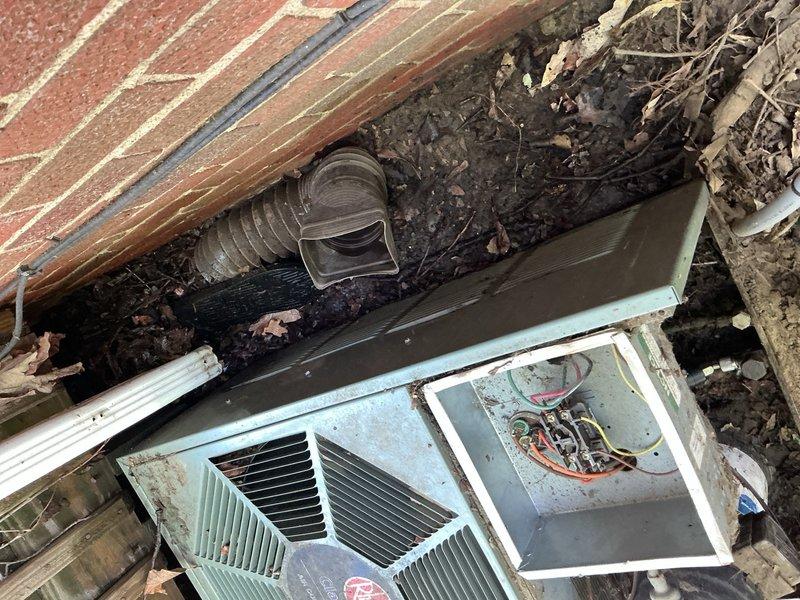 Responded to service call for insufficient airflow from 10+ year old air conditioning system with outdoor condenser unit located in basement area. Upon arrival, performed visual inspection of exterior condenser unit which revealed significant accumulation of leaves, organic debris, and dirt on and around equipment. Unit casing showed extensive weathering and age-related deterioration. Removed top panel to access internal components and assess operational status.

Discovered heavy debris buildup beneath and around condenser unit, including dead leaves and decomposed plant matter that had accumulated between unit and building foundation. Identified potential airflow restriction issues due to debris accumulation on fan grille and surrounding areas. Wooden mounting platform showed advanced deterioration from prolonged weather exposure.

Documented equipment condition through photographs showing exterior unit placement, internal component access, debris accumulation, and overall installatio