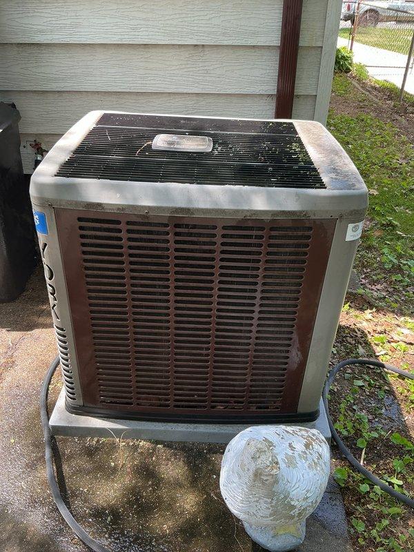 Completed routine air conditioning tune-up on outdoor condensing unit located in basement area. Performed comprehensive maintenance including inspection of compressor, condenser coils, refrigerant lines, and electrical connections. Unit showed signs of age with weathering and debris accumulation on protective grilles; cleaned top fan grille and cabinet exterior. Verified proper operation of condenser fan motor and checked refrigerant line connections for secure mounting. Inspected concrete pad for levelness and stability. System operational upon completion of maintenance service.