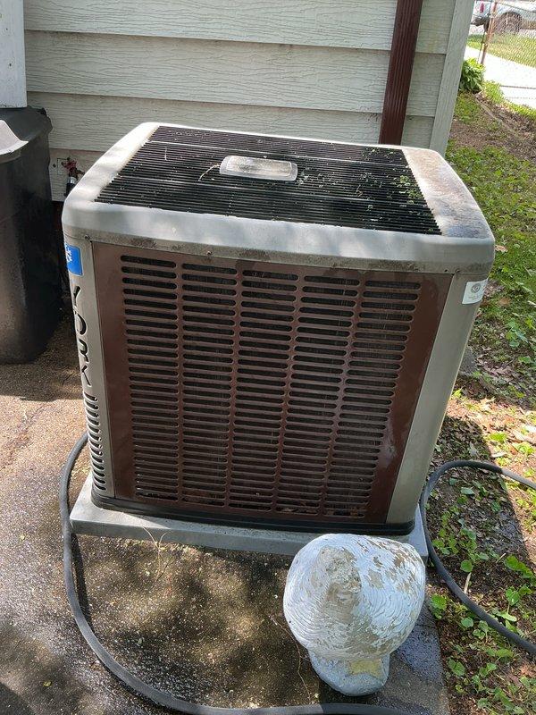 Completed routine air conditioning tune-up on outdoor condensing unit located in basement area. Performed comprehensive maintenance including inspection of compressor, condenser coils, refrigerant lines, and electrical connections. Unit showed signs of age with weathering and debris accumulation on protective grilles; cleaned top fan grille and cabinet exterior. Verified proper operation of condenser fan motor and checked refrigerant line connections for secure mounting. Inspected concrete pad for levelness and stability. System operational upon completion of maintenance service.
