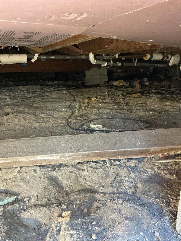 Responded to plumbing repair call for moisture issues in crawl space and wall cavity access. Upon inspection, discovered compromised drainage system with visible standing water and saturated soil throughout crawl space area. White PVC drainage piping showed signs of potential leakage or inadequate drainage, contributing to excessive moisture accumulation beneath structure. 

Created wall access opening to expose and inspect concealed plumbing infrastructure. Located black supply line and white PVC drain line running vertically through wall cavity. Secured both pipes with proper mounting clamps to prevent movement and potential future damage. Addressed compromised wall section and prepared opening for proper plumbing access and future maintenance requirements.

Documented crawl space conditions showing moisture intrusion affecting floor joists and insulation integrity. Recommended ongoing monitoring of drainage system performance and crawl space moisture levels to prevent structural dam