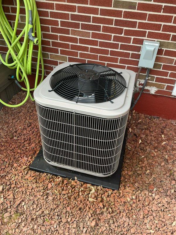 Completed comprehensive Gold AC inspection on residential cooling system under 10 years old with air handler located in basement. System confirmed operational and functioning properly at time of inspection. Inspected indoor air handler unit, ductwork connections, and outdoor condenser unit positioned on pad against exterior brick wall. Evaluated condenser cabinet condition, fan assembly operation, refrigerant line set, and electrical disconnect. Documented equipment configuration including water heater and furnace in mechanical room. Advised customer to maintain clear area around outdoor condenser unit, removing any debris or animal waste to ensure proper airflow and system efficiency.
