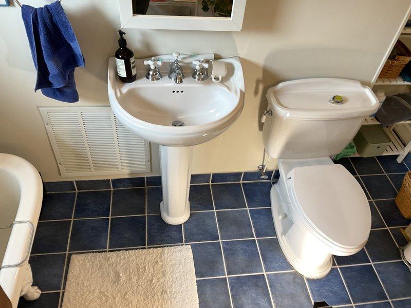 Completed toilet replacement in residential bathroom. Assessed existing pedestal sink installation for vanity conversion project, ensuring proper wall-mounting hardware and supply line configuration remain intact for future cabinet installation around fixture. Verified all shut-off valves, chrome supply lines, and drain connections are functioning properly and accessible for upcoming vanity retrofit work.