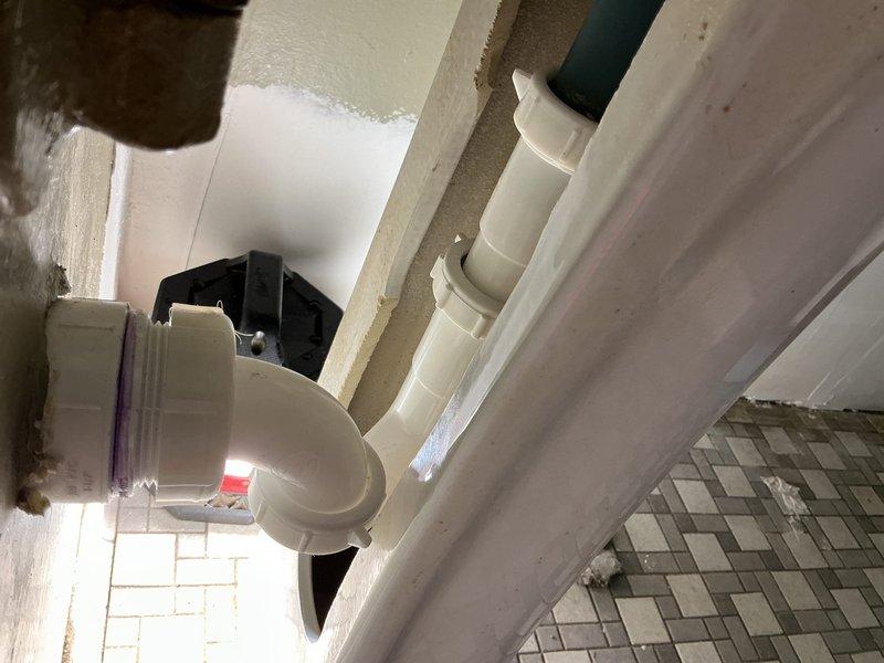 Performed camera inspection of residential plumbing system beneath bathroom vanity and exterior wall penetration. Documented P-trap configuration with white PVC piping, threaded connections, and drain components in good working condition, along with exterior drainage elbow fitting with proper wall sealant application.
