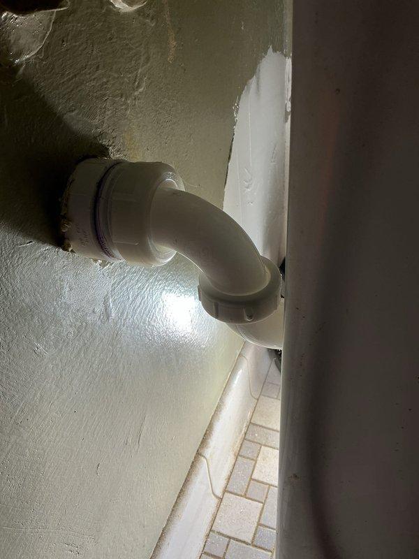 Performed camera inspection of residential plumbing system beneath bathroom vanity and exterior wall penetration. Documented P-trap configuration with white PVC piping, threaded connections, and drain components in good working condition, along with exterior drainage elbow fitting with proper wall sealant application.