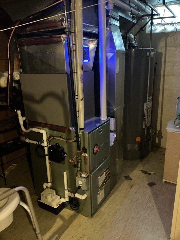 Responded to warranty call for one-month-old cooling system producing banging noise every 5-10 minutes upon startup. Inspected basement-installed HVAC equipment including air handler and associated components. Evaluated White-Rodgers programmable thermostat operation and system cycling patterns. Documented equipment configuration with furnace/air handler unit, condensate pump assembly, and PVC drainage connections. Identified and resolved mechanical issue causing intermittent noise during compressor engagement. Verified proper system operation, confirmed quiet startup cycles, and tested thermostat programming functionality to ensure normal cooling performance.