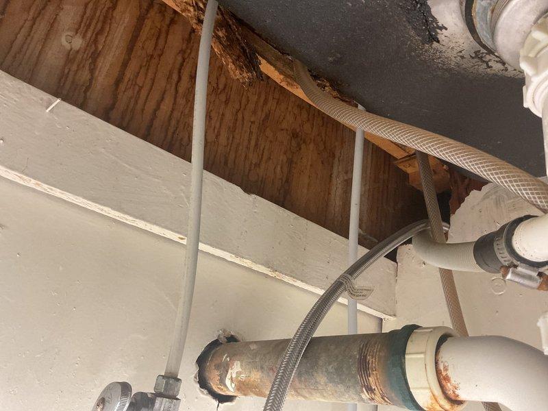 Responded to kitchen faucet drip in 30-year-old home. Inspected chrome dual-handle faucet with pull-down spray head mounted on dark sink basin. Examined supply lines and connections in basement crawlspace, noting aged piping with visible corrosion on metal fittings. Addressed leak source, tightened connections, and verified proper operation of faucet handles and spray function. System tested and confirmed no active dripping upon completion.