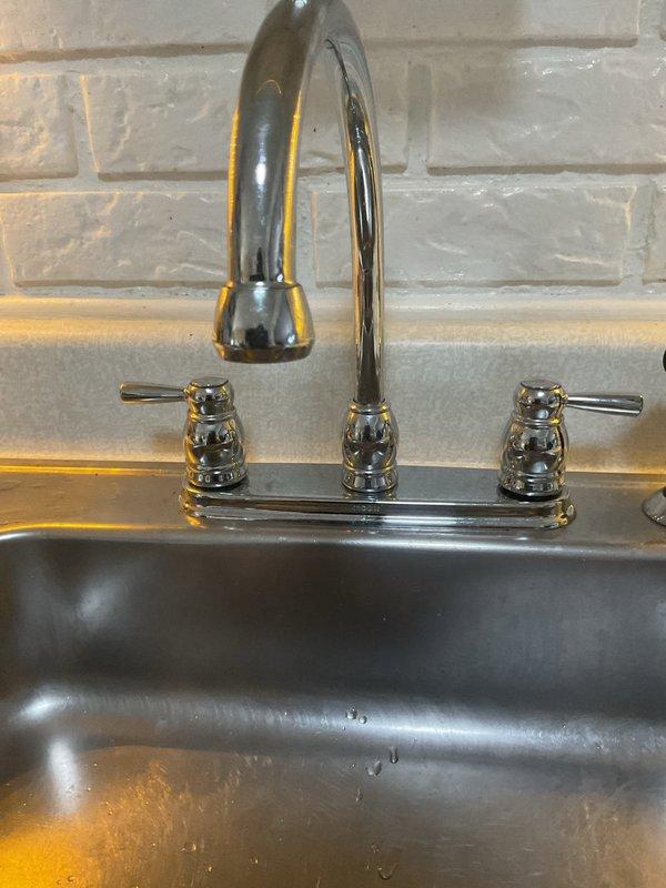 Responded to kitchen faucet drip in 30-year-old home. Inspected chrome dual-handle faucet with pull-down spray head mounted on dark sink basin. Examined supply lines and connections in basement crawlspace, noting aged piping with visible corrosion on metal fittings. Addressed leak source, tightened connections, and verified proper operation of faucet handles and spray function. System tested and confirmed no active dripping upon completion.