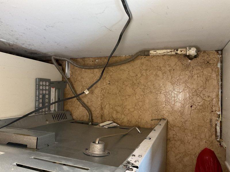 Responded to natural gas leak emergency behind kitchen oven after utility company confirmed leak and shut off gas supply to 1962-built home. Conducted thorough visual inspection of gas piping system in affected area, identifying severely corroded gas supply lines with compromised integrity due to age and deterioration. Documented existing conditions showing extensive rust and corrosion on vertical pipe assembly and fittings, with deteriorated paint coating exposing compromised metal surfaces. Assessed flexible gas connector to range and surrounding infrastructure for additional leak points and safety concerns.