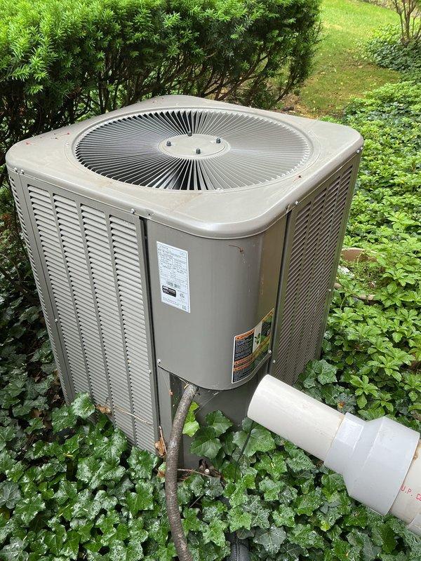 Completed comprehensive Gold Plan AC inspection on a 2-year-old residential air conditioning system with outdoor condenser unit and basement-located air handler. Performed thorough visual assessment of exterior condenser unit, confirming proper operation of all components including fan assembly and ventilation systems. Inspected unit housing, verified manufacturer labels and safety information were intact and legible. Examined condensate drainage system including PVC discharge line for proper function and clear flow. Assessed unit placement and surrounding clearances, noting adequate airflow access through louvered panels. Documented equipment condition with photographic records showing well-maintained condenser with normal outdoor weathering for age. All system components operating within normal parameters at time of inspection.