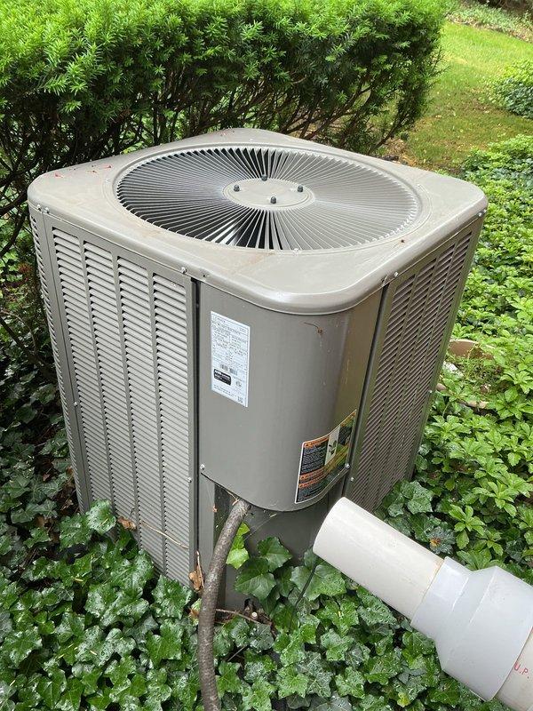 Completed comprehensive Gold Plan AC inspection on a 2-year-old residential air conditioning system with outdoor condenser unit and basement-located air handler. Performed thorough visual assessment of exterior condenser unit, confirming proper operation of all components including fan assembly and ventilation systems. Inspected unit housing, verified manufacturer labels and safety information were intact and legible. Examined condensate drainage system including PVC discharge line for proper function and clear flow. Assessed unit placement and surrounding clearances, noting adequate airflow access through louvered panels. Documented equipment condition with photographic records showing well-maintained condenser with normal outdoor weathering for age. All system components operating within normal parameters at time of inspection.