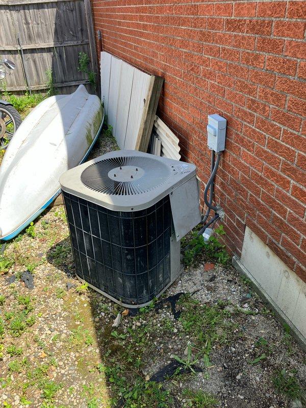 Completed comprehensive site assessment for full HVAC system replacement, including both outdoor condensing unit and indoor furnace/air handler. Inspected existing outdoor AC unit positioned on concrete pad in side yard, noting weathered condition, electrical disconnect box, and refrigerant line connections to brick wall. Evaluated indoor furnace installation in basement utility area, including existing humidifier integration, ductwork configuration, and overall system layout. Documented current equipment specifications, electrical connections, duct transitions, and installation conditions through detailed photography. Assessed site accessibility, clearance requirements, and utility connections to determine replacement specifications and installation requirements for new complete HVAC system.