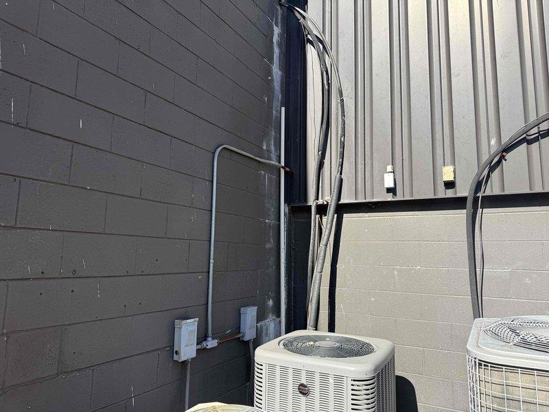 Responded to commercial A/C service call for two units located near lunch room area accessible via stairs. Performed diagnostic inspection on malfunctioning unit, documenting interior ductwork condition and identifying debris accumulation within cylindrical chamber. Inspected outdoor condenser units and associated refrigerant lines, electrical connections, and mounting components. Photographed equipment condition for repair estimate preparation on one unit while assessing operational status of second unit.