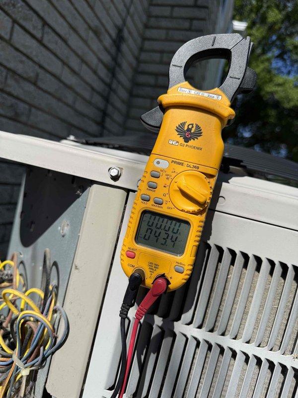 Completed comprehensive Gold AC inspection on 13-year-old residential air conditioning system with basement-located air handler. Performed electrical diagnostics on outdoor condenser unit using clamp meter to verify proper amperage draw and system performance. Inspected condenser coil fins, confirmed unit operation, and verified adequate clearance around equipment, noting minor weathering consistent with age but overall functional condition of system.