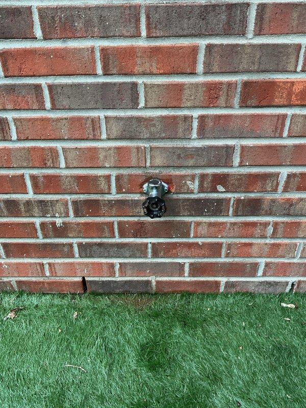 Installed new exterior hose bib on commercial building's red brick wall, mounting the frost-proof fixture at appropriate height above grade level with proper drainage slope. Completed interior rough-in plumbing connections through wall assembly near glass block window, ensuring secure water supply line installation and proper shut-off valve placement for seasonal maintenance access.