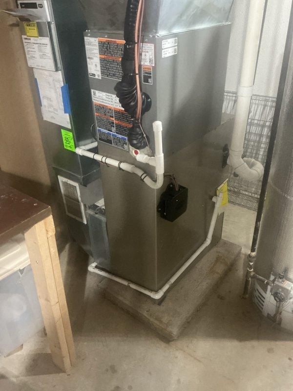 Completed installation of a 2-ton air conditioning system with matching evaporator coil. Indoor air handler was mounted on concrete platform in basement utility area with refrigerant lines properly routed and connected. Outdoor condensing unit was positioned at rear of property adjacent to brick wall with electrical disconnect and conduit professionally installed. All mechanical, electrical, and air conditioning permits were requested and system was reconnected to existing infrastructure. White PVC condensate drain lines were installed and secured, copper refrigerant lines were properly insulated and routed, and all manufacturer specifications and warning labels remain visible for future service reference. System was tested for proper operation and left in full working condition.