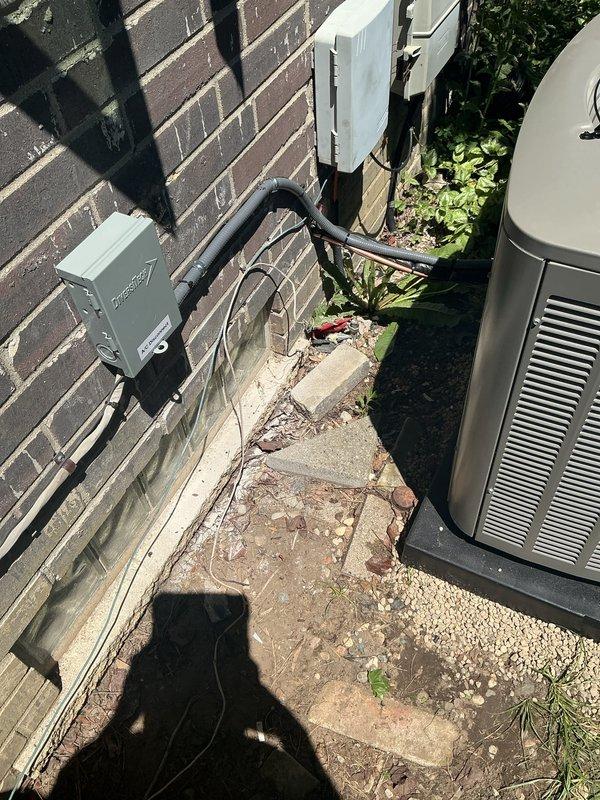 Completed installation of a 2-ton air conditioning system with matching evaporator coil. Indoor air handler was mounted on concrete platform in basement utility area with refrigerant lines properly routed and connected. Outdoor condensing unit was positioned at rear of property adjacent to brick wall with electrical disconnect and conduit professionally installed. All mechanical, electrical, and air conditioning permits were requested and system was reconnected to existing infrastructure. White PVC condensate drain lines were installed and secured, copper refrigerant lines were properly insulated and routed, and all manufacturer specifications and warning labels remain visible for future service reference. System was tested for proper operation and left in full working condition.