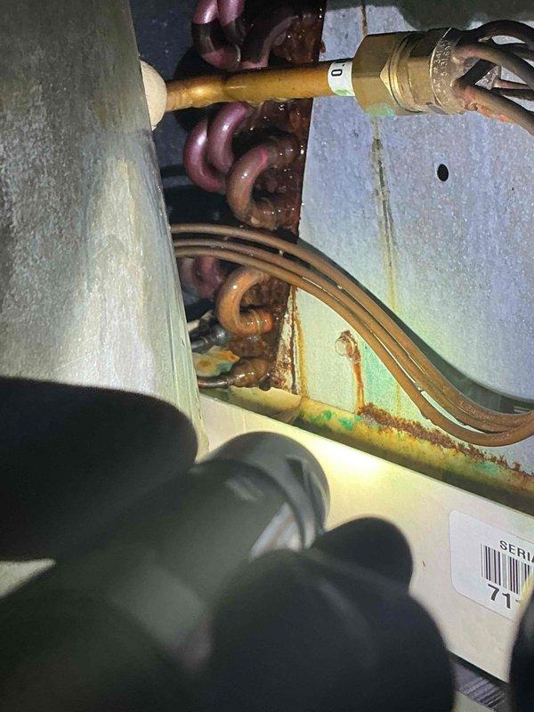 Responded to call for basement AC unit freezing up. Upon inspection, found evaporator coil experiencing ice buildup due to restricted airflow. Identified heavily corroded copper coil sections and deteriorated components showing significant oxidation and rust accumulation from moisture exposure. Assessed refrigerant lines, connections, and housing panels for integrity. Documented equipment condition with photos showing aged components, corroded coils, and compromised metal surfaces requiring attention to prevent continued freeze-up issues.