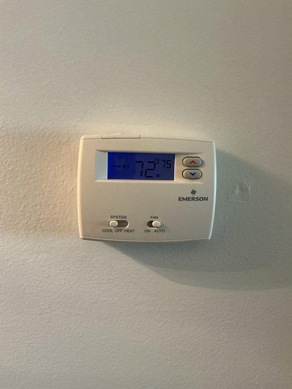 Completed comprehensive Gold AC Inspection on a two-year-old air conditioning system located on the upstairs porch. Performed full system tune-up including inspection of the air handler unit, verified thermostat operation showing 72°F setpoint with proper display functionality, checked condensate drainage system with blue PVC piping and flexible discharge line, and inspected all mechanical components. Verified Emerson programmable thermostat controls functioning correctly in cooling mode with auto fan settings. Examined equipment labels and specifications, confirmed all connections secure, and found system operating within normal parameters with no issues identified. Unit requires no immediate repairs and is ready for continued seasonal operation.