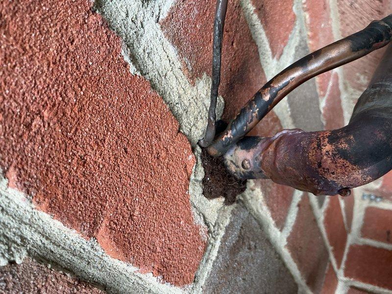 Responded to no cooling complaint on second floor air conditioning system. Upon inspection, identified refrigerant line penetration issues at exterior wall with deteriorated insulation and compromised sealing. Corroded lineset penetration through brick exterior showed significant weathering and inadequate protection from elements. Re-insulated refrigerant lines with proper foam insulation sleeve at wall penetration point and sealed openings with appropriate materials to prevent air infiltration and protect copper lines from environmental damage. System restored to proper cooling operation.