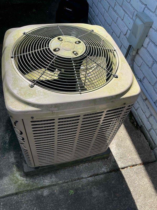 Completed comprehensive Gold-level air conditioning inspection on 15-year-old residential HVAC system with air handler located in basement. Performed thorough visual assessment of outdoor condenser unit, which showed significant age-related wear including pollen accumulation, surface weathering, and dirt buildup on housing and fan guard assembly. Inspected fan assembly, protective grille, ventilation slats, and electrical connections. Unit confirmed operational at time of inspection. Documented equipment condition through photographic records showing exterior components, top fan assembly with protective guard, and overall system placement on concrete pad adjacent to structure. System continues to function despite visible signs of aging and environmental exposure consistent with 15 years of outdoor operation.