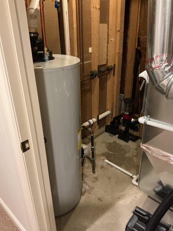 Completed installation of a 50-gallon Bradford White power vent water heater in residential utility space. Installed unit includes copper supply piping connections at top of tank, PVC intake and exhaust venting system, pressure relief valve, and complete plumbing manifold with shut-off valves at base. All connections properly secured and tested for leaks, with unit positioned on concrete floor against framed wall structure and electrical controls mounted for code-compliant operation.
