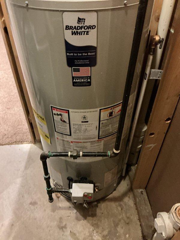 Completed installation of a 50-gallon Bradford White power vent water heater in residential utility space. Installed unit includes copper supply piping connections at top of tank, PVC intake and exhaust venting system, pressure relief valve, and complete plumbing manifold with shut-off valves at base. All connections properly secured and tested for leaks, with unit positioned on concrete floor against framed wall structure and electrical controls mounted for code-compliant operation.