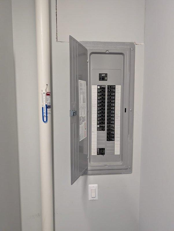 Completed electrical service work at residential property involving circuit breaker panel inspection and outlet installation. Accessed main electrical panel mounted in utility area adjacent to water heater, verified proper breaker configuration and panel labeling. Installed new electrical outlet in corner area near floor level with dark wood flooring and tiled wall section, ensuring proper grounding and secure mounting to meet current electrical code requirements. Connected power supply, tested outlet functionality, and confirmed safe operation of all installed components.