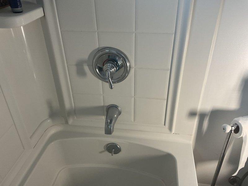Completed on-site assessment for bathtub replacement in first floor bathroom of 1960s ranch-style home. Documented existing white subway-tiled shower/tub enclosure with chrome fixtures including temperature control valve, tub spout, and overhead shower head. Evaluated current bathtub condition, wall-mounted grab bar placement, and recessed shelf niches built into tile surround. Photographed existing plumbing fixtures, tile work, and bathroom configuration to provide accurate estimate for tub removal and replacement project.
