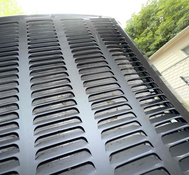 Completed comprehensive Gold AC inspection on 12-year-old residential air conditioning system with air handler located in basement. Performed thorough evaluation of outdoor condenser unit positioned against exterior brick wall, confirming operational status and inspecting all accessible components including top fan grille, protective louvers, and housing integrity. Observed minor weathering consistent with equipment age but verified unit remains structurally sound and functional. Noted presence of landscaping vegetation near condenser base and advised customer that area surrounding unit should be kept clear of debris and animal waste to maintain proper airflow and prevent potential performance issues. Documented equipment condition through photographic inspection showing intact protective grilles, mesh screening, and ventilation louvers. All inspection protocols completed per Gold service standards.
