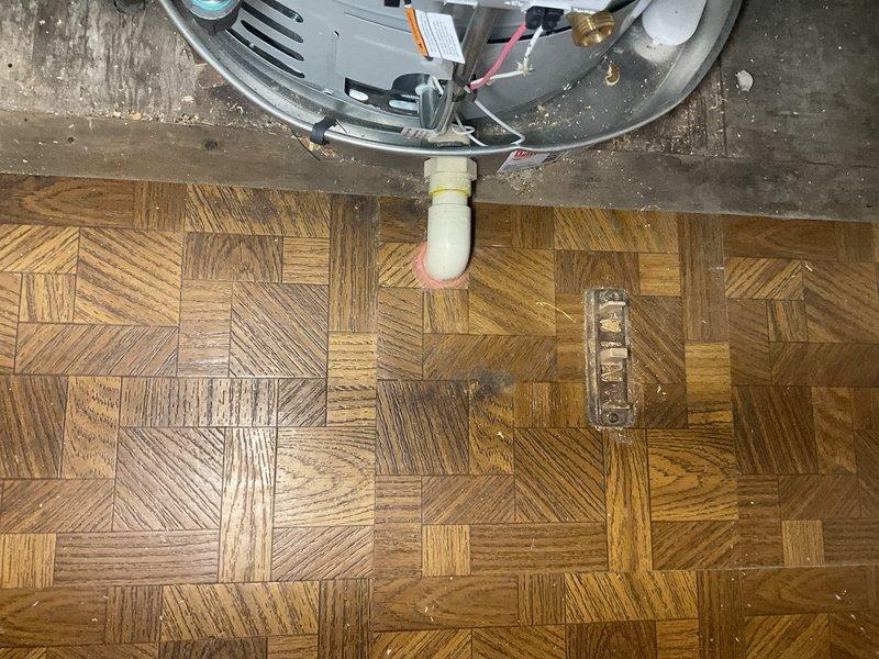 Responded to a flame violation notice regarding improper water heater installation. Terminated and properly routed the drain pan discharge line to the crawl space as required by code. Addressed chimney penetration issues by applying mortar around the ductwork where it passes through the ceiling to seal gaps and prevent potential hazards. Documentation photos captured the water heater unit with exposed drain line termination on parquet flooring and the metal ductwork penetration through the ceiling showing previous water damage and staining around the penetration points that required sealing.