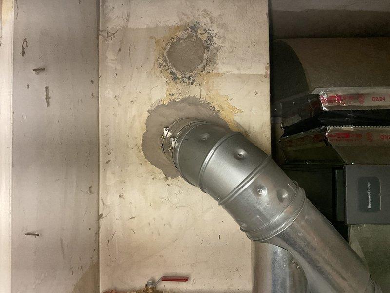Responded to a flame violation notice regarding improper water heater installation. Terminated and properly routed the drain pan discharge line to the crawl space as required by code. Addressed chimney penetration issues by applying mortar around the ductwork where it passes through the ceiling to seal gaps and prevent potential hazards. Documentation photos captured the water heater unit with exposed drain line termination on parquet flooring and the metal ductwork penetration through the ceiling showing previous water damage and staining around the penetration points that required sealing.