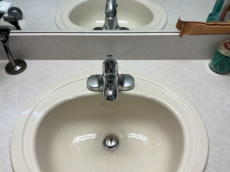 Completed installation estimate for two new faucets in a 25-year-old residential property. Assessed bathroom vanity with dual oval porcelain sinks requiring chrome single-handle faucet replacement and evaluated kitchen double-basin stainless steel sink for brushed nickel pull-down faucet installation. Documented existing plumbing configurations, verified water supply line accessibility, and photographed current fixture conditions to provide accurate material and labor specifications for the requested upgrades.