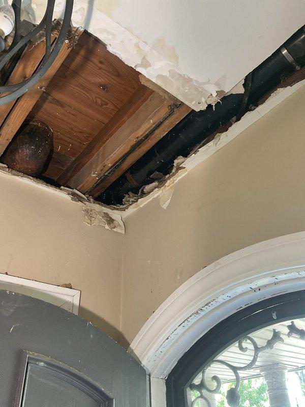 Responded to plumbing emergency involving compromised ceiling and exposed piping system. Upon arrival, identified significant water damage to interior ceiling with structural breach exposing wooden joists and subflooring. Large black drain pipe was accessible through damaged drywall, with visible water staining indicating previous moisture intrusion. 

Assessed the extent of damage and determined repair scope, including exposed plumbing infrastructure and affected building materials. Documented conditions showing torn drywall edges, discolored ceiling surfaces, and compromised structural elements requiring remediation. Provided repair estimate and obtained approval to proceed with necessary corrections to restore proper function and structural integrity.