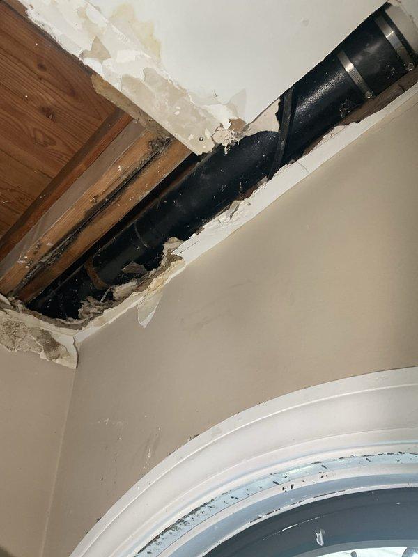 Responded to plumbing emergency involving compromised ceiling and exposed piping system. Upon arrival, identified significant water damage to interior ceiling with structural breach exposing wooden joists and subflooring. Large black drain pipe was accessible through damaged drywall, with visible water staining indicating previous moisture intrusion. 

Assessed the extent of damage and determined repair scope, including exposed plumbing infrastructure and affected building materials. Documented conditions showing torn drywall edges, discolored ceiling surfaces, and compromised structural elements requiring remediation. Provided repair estimate and obtained approval to proceed with necessary corrections to restore proper function and structural integrity.