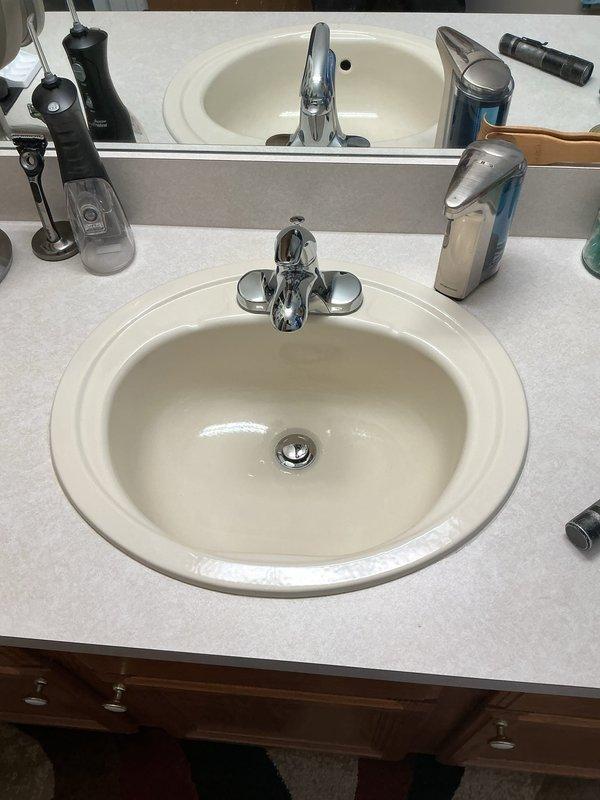 Responded to emergency service call for leaking faucet at 25-year-old residential property. Successfully installed two new faucet fixtures—one chrome bathroom vanity faucet at double-sink vanity with speckled gray countertop, and one kitchen faucet connected to existing garbage disposal and dishwasher tailpiece assembly with PVC P-trap configuration. All connections tested and verified leak-free with proper water pressure and drainage function.