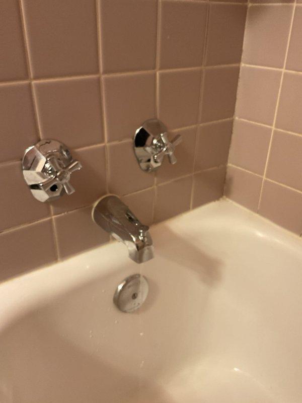 Responded to service call for bathtub leak and clogged bathroom sink. Upon inspection, identified leak source requiring access panel installation in wall cavity to reach supply lines. Cut access opening in drywall to expose plumbing infrastructure, revealing vertical copper supply pipes and connection points behind tub fixture. Addressed leak at pipe connection, cleared sink drainage obstruction, and verified proper operation of three-handle tub fixture assembly and chrome spout. Both fixtures tested and confirmed operational upon completion.