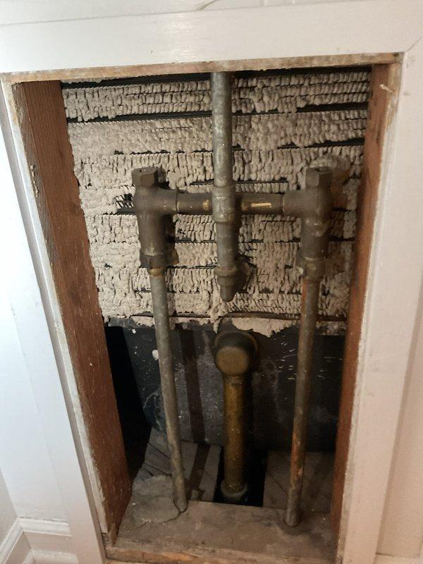 Responded to service call for bathtub leak and clogged bathroom sink. Upon inspection, identified leak source requiring access panel installation in wall cavity to reach supply lines. Cut access opening in drywall to expose plumbing infrastructure, revealing vertical copper supply pipes and connection points behind tub fixture. Addressed leak at pipe connection, cleared sink drainage obstruction, and verified proper operation of three-handle tub fixture assembly and chrome spout. Both fixtures tested and confirmed operational upon completion.
