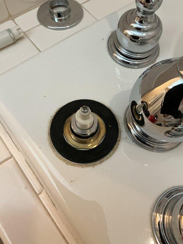 Responded to service call for bathroom plumbing repairs involving faucet and drainage issues. Replaced drain plug assembly and addressed loose water spout on bathroom sink by disassembling faucet components, removing valve stem cartridge, and securing mounting hardware with new gaskets and seals. Completed replacement of tub fixtures as requested. During inspection, identified water leakage beneath flooring through access cutout, revealing compromised PVC drain trap connection with visible water accumulation on subfloor. Documented plumbing conditions with photographic evidence showing exposed valve assemblies, chrome fixtures, and underneath drainage system requiring attention to prevent further water damage.