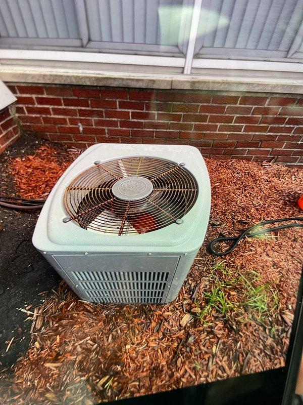 Completed comprehensive annual maintenance inspection on 20-year-old air conditioning system located at rear of property. Performed standard AC tune-up procedures including visual inspection of condenser unit, verification of fan operation, examination of electrical connections, and assessment of overall system condition. Unit showed typical age-related surface wear but remained structurally sound with intact metal casing, functional louver vents, and proper grille protection. Cleared surrounding area of debris and leaves to ensure adequate airflow around condenser. All manufacturer safety labels present and legible. System operational upon completion of maintenance service.