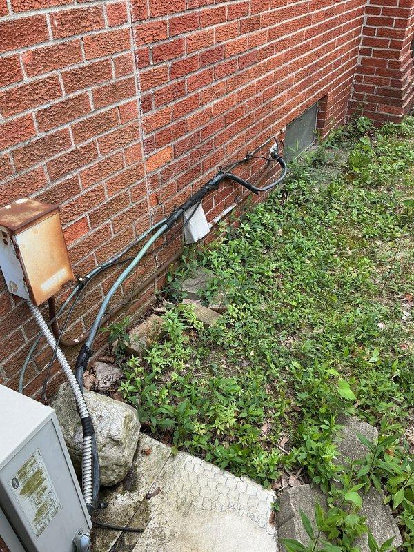 Completed on-site assessment of existing outdoor air conditioning condenser unit for replacement estimate. Unit exhibited significant weathering, rust, and oxidation throughout metal components and housing, with yellowed and deteriorated top cover indicating extended service life. Inspected electrical disconnect box, refrigerant line set with insulation, and conduit runs along brick exterior wall. Documented equipment condition, installation configuration, and utility connections. Photographed existing system components including concrete pad foundation with vegetation overgrowth. Provided comprehensive replacement estimate for new AC system installation.