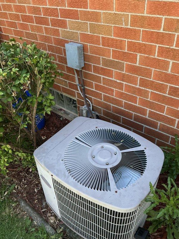 Responded to service call for non-cooling AC system located in backyard. Upon arrival, located outdoor condenser unit positioned against exterior brick wall. Performed diagnostic testing on electrical components using digital multimeter to check voltage and system operation. Accessed electrical disconnect box and control panel to test capacitor and verify proper electrical readings across circuits. Based on diagnostic findings showing 7.39 volts at tested connection point, identified electrical issue preventing compressor operation. Unit showed signs of age and outdoor weathering but condenser fan assembly and housing remained structurally sound. Completed electrical troubleshooting and testing procedures to isolate root cause of system failure.