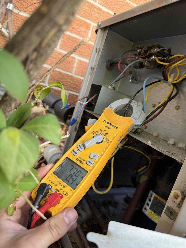 Responded to service call for non-cooling AC system located in backyard. Upon arrival, located outdoor condenser unit positioned against exterior brick wall. Performed diagnostic testing on electrical components using digital multimeter to check voltage and system operation. Accessed electrical disconnect box and control panel to test capacitor and verify proper electrical readings across circuits. Based on diagnostic findings showing 7.39 volts at tested connection point, identified electrical issue preventing compressor operation. Unit showed signs of age and outdoor weathering but condenser fan assembly and housing remained structurally sound. Completed electrical troubleshooting and testing procedures to isolate root cause of system failure.