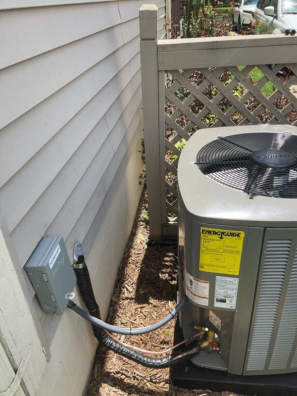 Completed installation of 3-ton air conditioning system with matching evaporator coil on left side of residence. Unit positioned on concrete pad against decorative lattice fence, with electrical disconnect box mounted on exterior wall and refrigerant lines properly insulated and routed through mulched side yard. All mechanical, electrical, and AC permits obtained and system reconnected per code requirements.