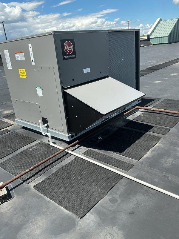 Completed installation of Rheem commercial rooftop unit (RTU) on flat membrane roof system. Unit was properly positioned and secured with appropriate walkway pads installed for maintenance access, all electrical connections completed, and weatherproofing verified per manufacturer specifications. Equipment tested and confirmed operational with no visible defects or installation issues.
