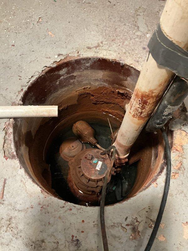 Completed new sump pump installation in basement of 55-year-old residence with no prior system in place. Excavated and installed sump basin in concrete floor, mounted submersible pump with discharge piping routed vertically through copper pipe assembly, and connected electrical supply with wall-mounted control switch for automatic operation to prevent basement flooding.