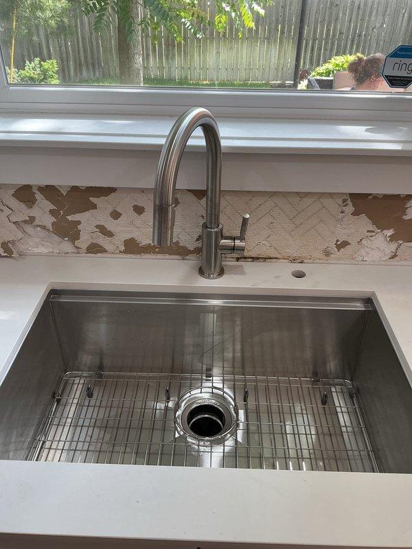 Completed continuation service on multiple plumbing fixtures throughout the residence, including four bathroom faucets, kitchen faucet, kitchen water spigot, and garbage disposal. Inspected and serviced kitchen sink installation featuring single-handle pull-down faucet with brushed stainless steel finish and verified proper operation of black garbage disposal unit with associated PVC P-trap drainage system and electrical connections. All fixtures tested and confirmed to be functioning properly upon completion.