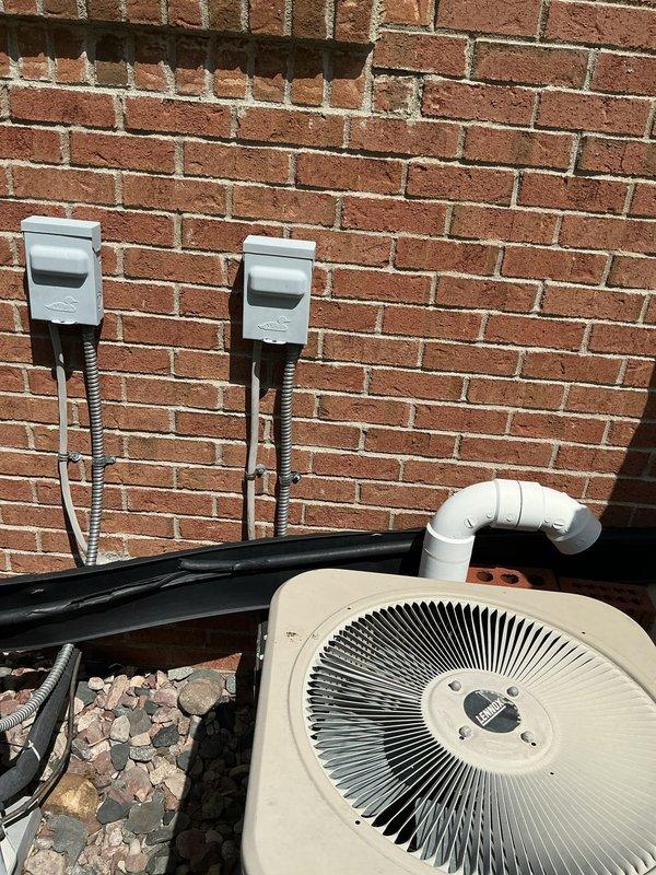 Completed full replacement of 20+ year-old outdoor air conditioning system with new condenser unit installed on gravel pad against exterior brick wall. New installation includes proper electrical disconnect boxes mounted to wall with conduit runs, PVC refrigerant line connections, and dual-unit configuration for enhanced cooling capacity. System tested and operational upon completion.