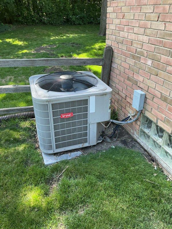 Completed comprehensive Gold AC Inspection on Bryant residential air conditioning system. Performed full system evaluation including outdoor condenser unit positioned on concrete pad against building exterior and indoor air handler cabinet located in mechanical room alongside Bryant furnace and water heater. Conducted standard tune-up procedures including visual inspection of condenser coil, fan operation verification, electrical connection assessment, and refrigerant line examination. Verified proper clearances around outdoor unit, checked mounting stability on concrete pad, and inspected electrical conduit connections from building to unit. Evaluated indoor components including ductwork connections and air handler operation. System operational at time of inspection with no immediate repairs required. Unit age unknown per service request. Documented equipment condition through photographic records showing installation configuration and component placement for future service reference.