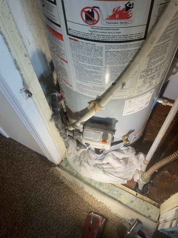 Responded to service call for leaking State Industries ProLine tanked water heater in mobile home installation, originally installed in 2018. Upon inspection, confirmed active leak at tank base with visible water damage and corrosion on copper piping connections. Noted absence of dedicated shut-off valve for water heater, requiring main water supply to home to be shut off for any service work. Documented warranty discrepancy between customer records indicating 10-year tank/5-year labor coverage and company records showing 6-year tank warranty. Photographed unit condition, piping connections, temperature and pressure relief valve assembly, and evidence of mineral deposits and copper oxidation on fittings. Tank installed in confined utility closet space with standard residential venting and plumbing connections. Recommended immediate attention due to active leak and lack of isolation valve for future service accessibility.